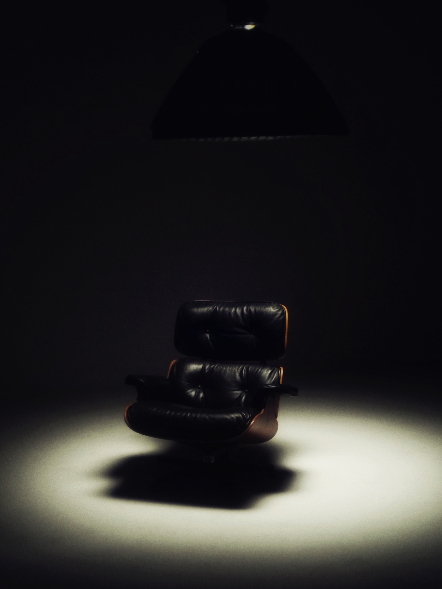 A spotlit black leather lounge chair against a dark background