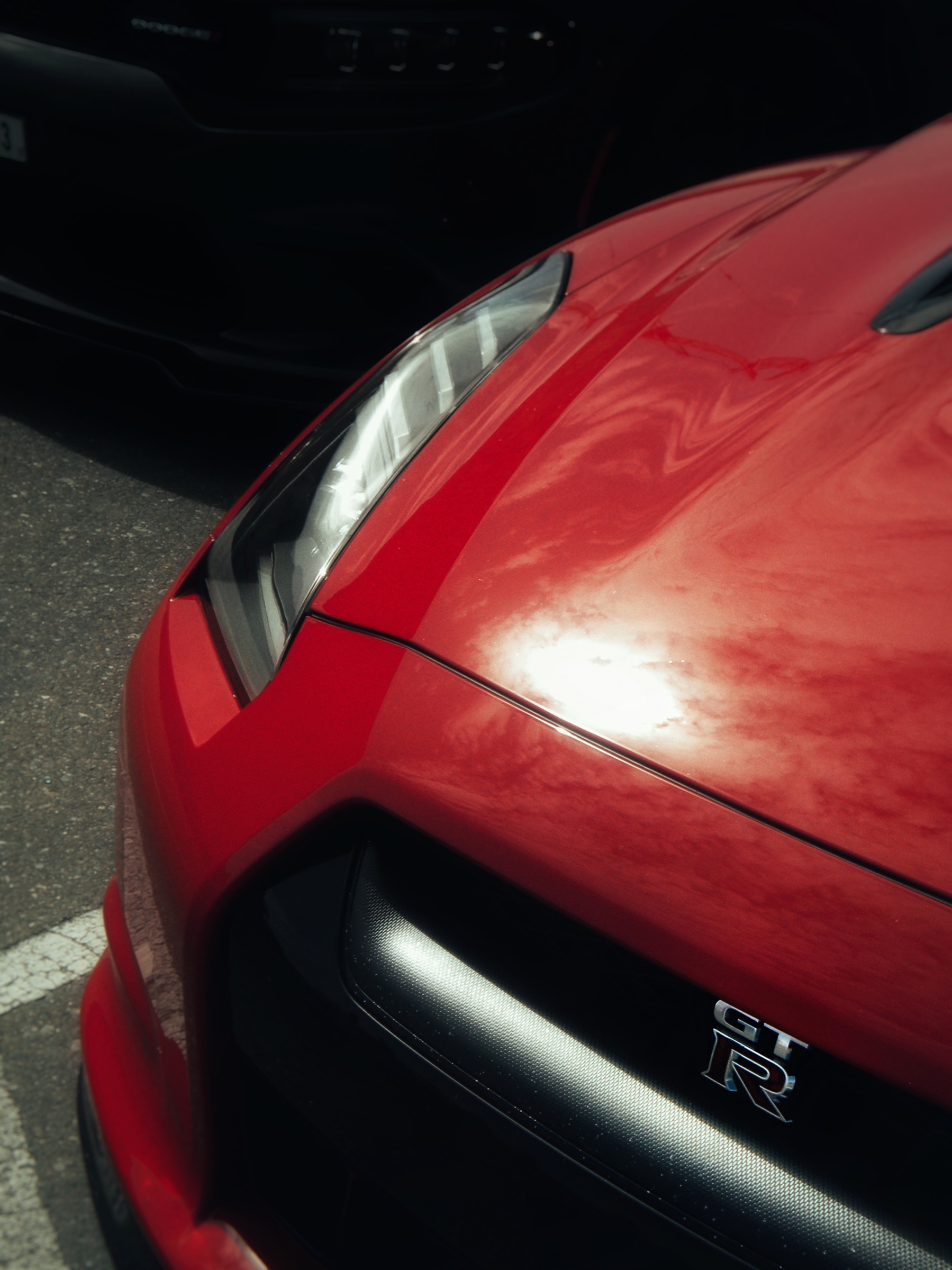 Macro study of a red car's hood and headlight, reflected sky in the paintwork